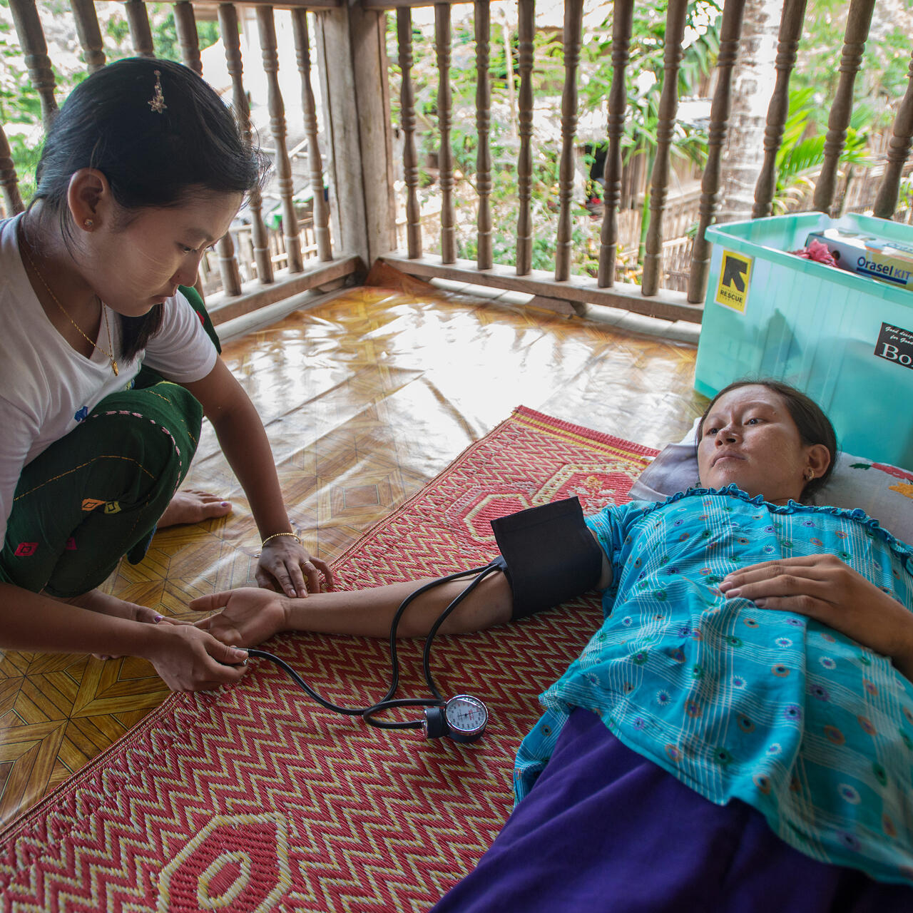 An IRC health worker takes the blood pressure of a female patient lying on a mat on the floor in Thailand.