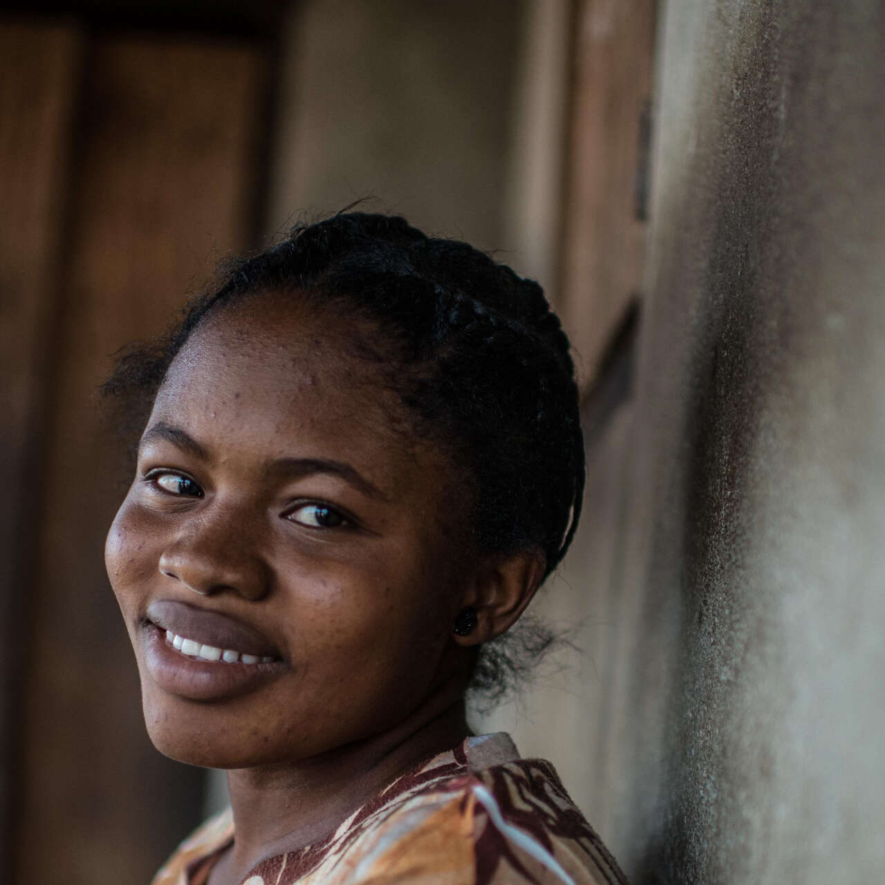 A woman stands against a wall and smiles.