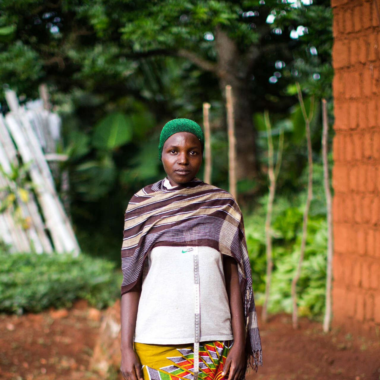 A woman with a green hat poses for a photo outside a home in Burundi.