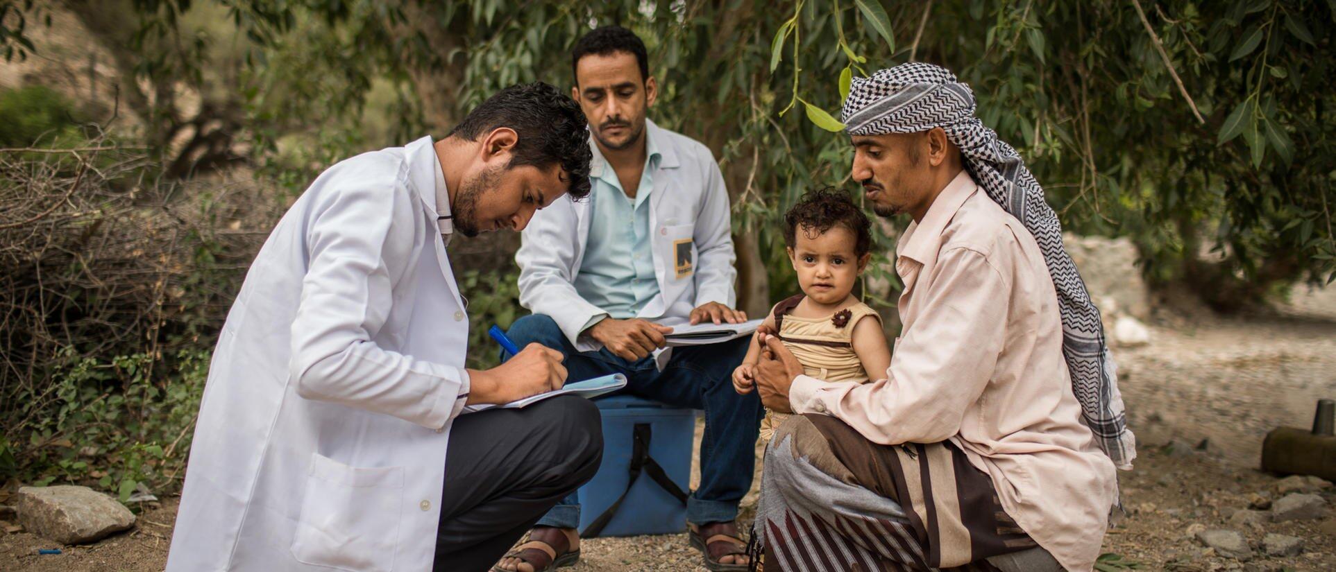 Two men taking notes while sitting with a child and his father