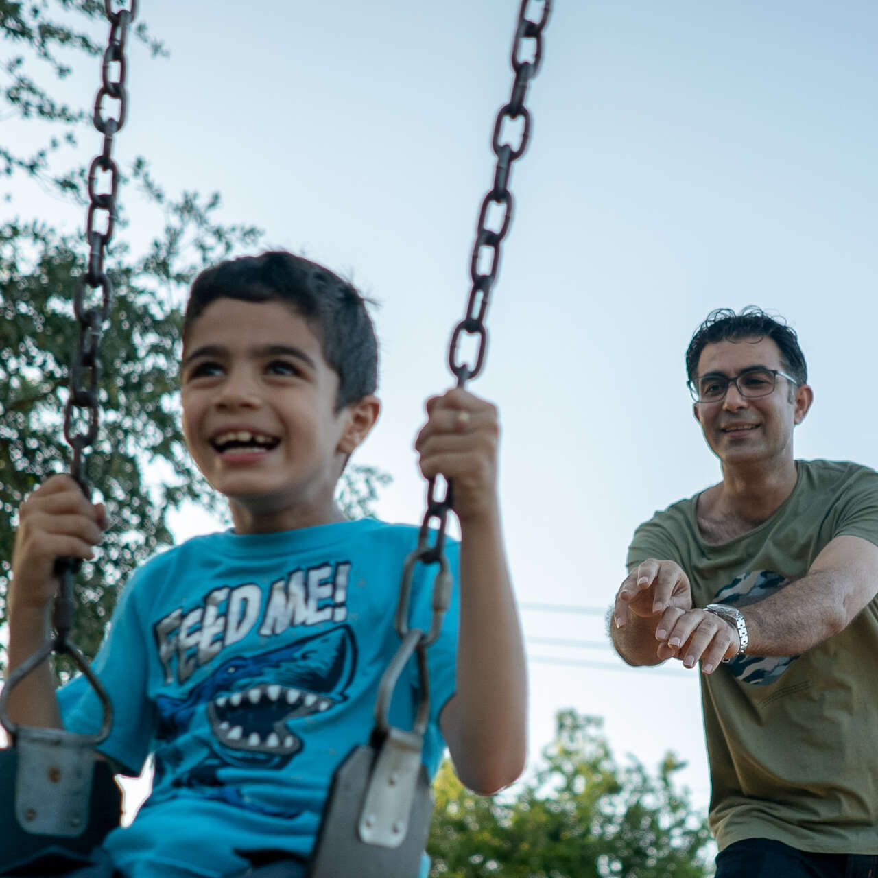 A man pushes a boy in a swing.