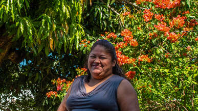 A woman stands in front of a blossoming tree and smiles for a photo.