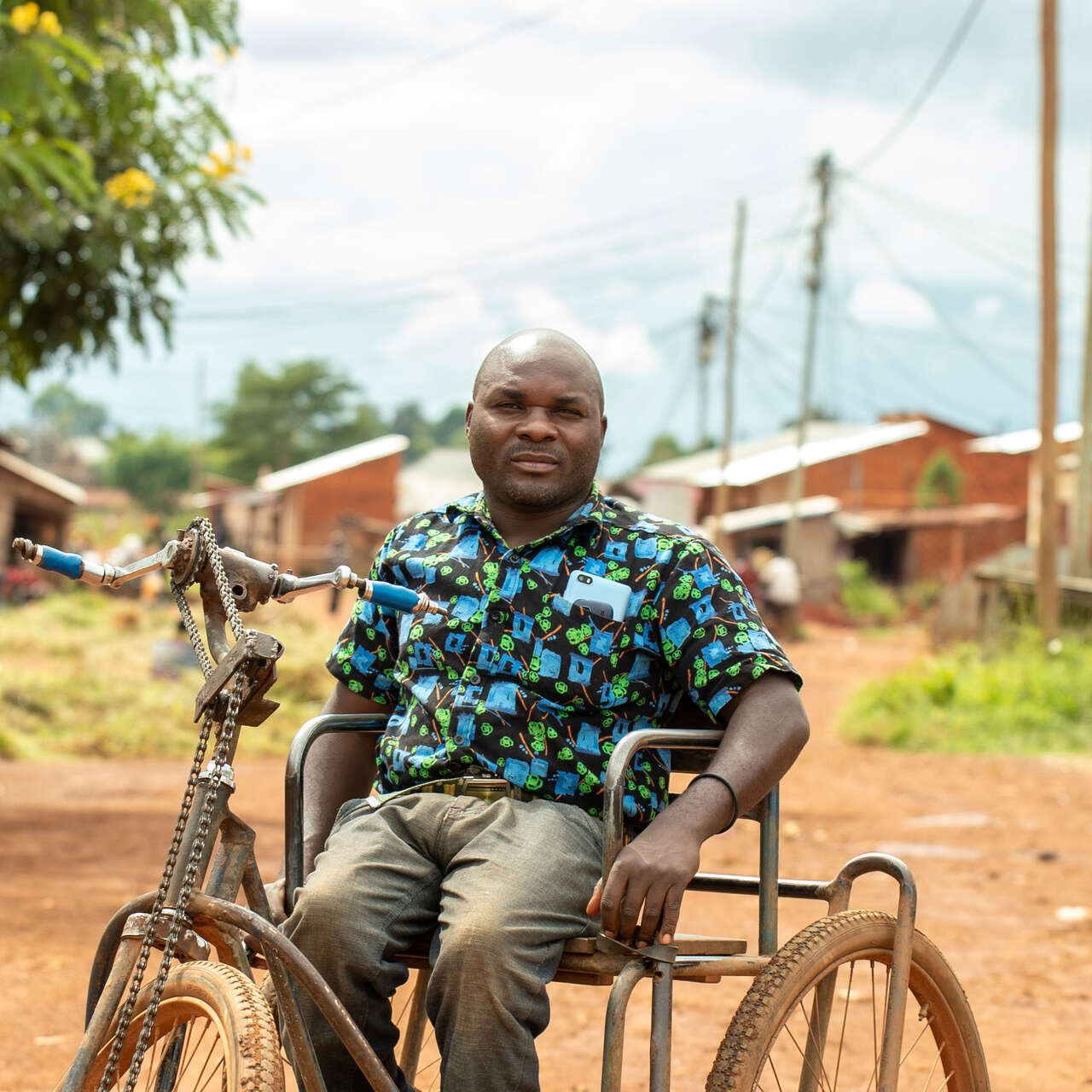 A man poses for a photo while sitting in a wheelchair and hand-cranked bicycle.