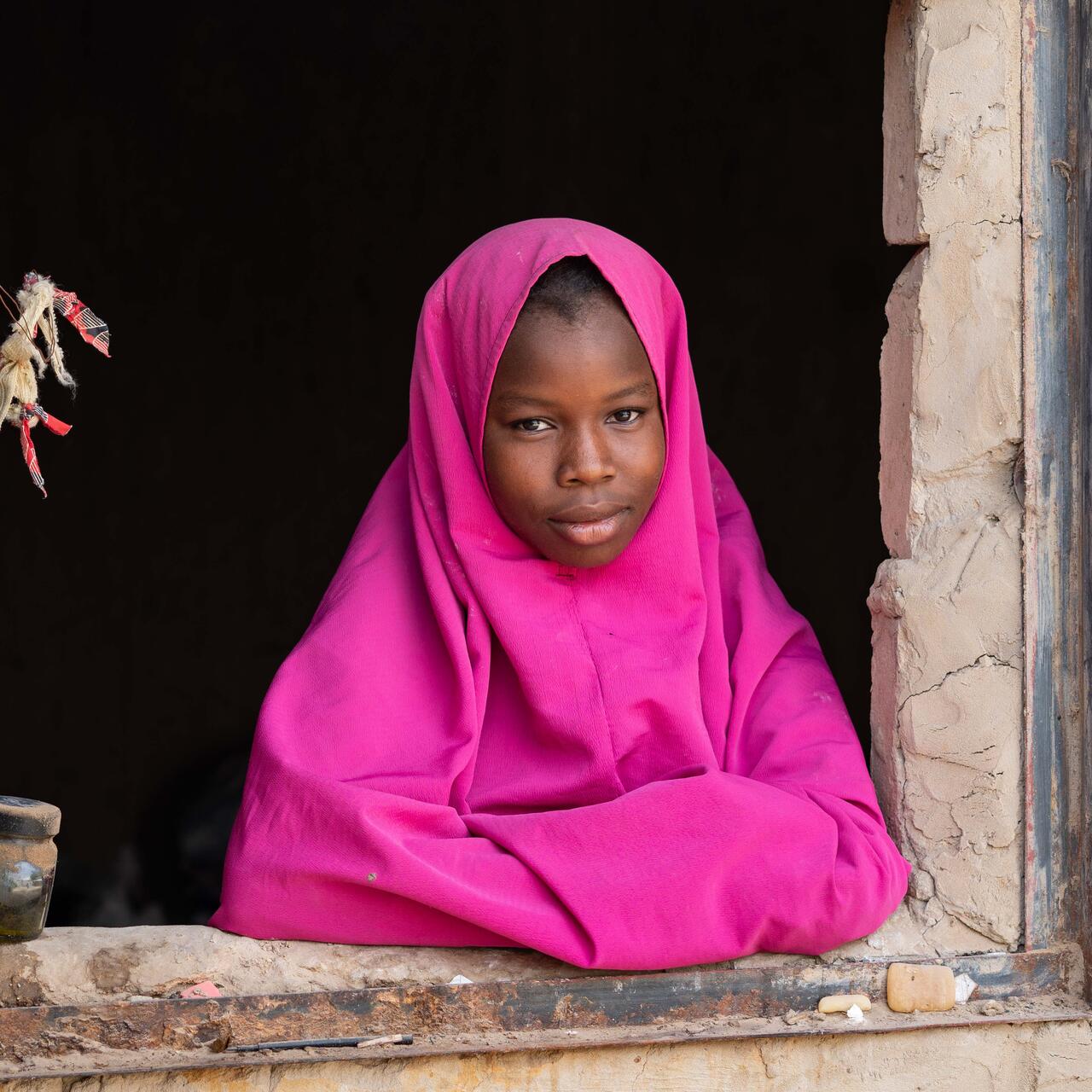 A girl poses for a picture while leaning out of a window sill.