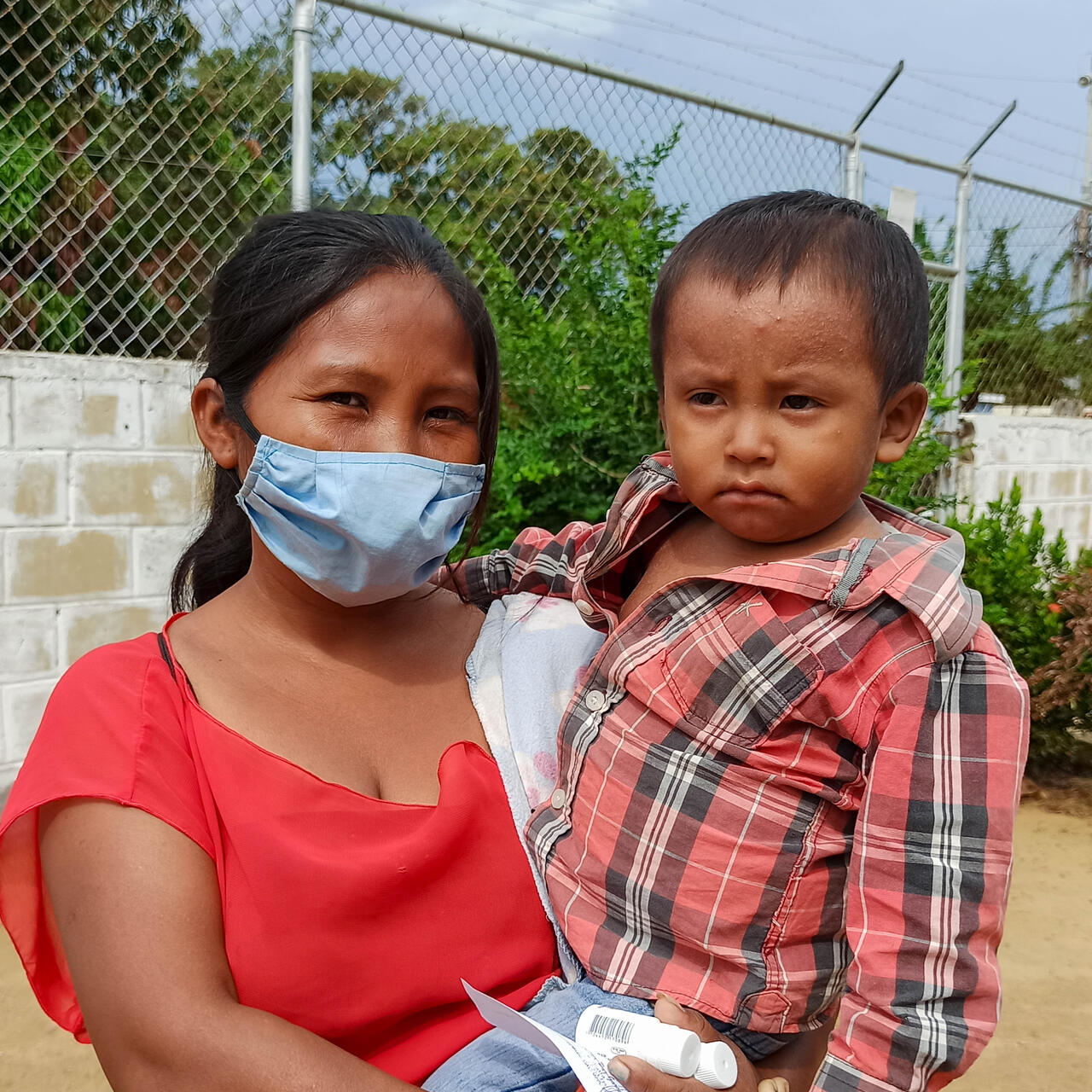 A mother holds her son and the pair pose for a photo outdoors.