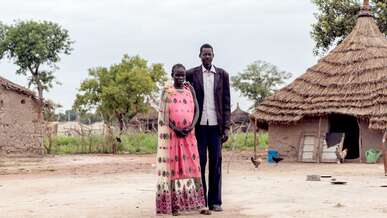 A man and a woman pose for a portrait in front of their home in South Sudan.