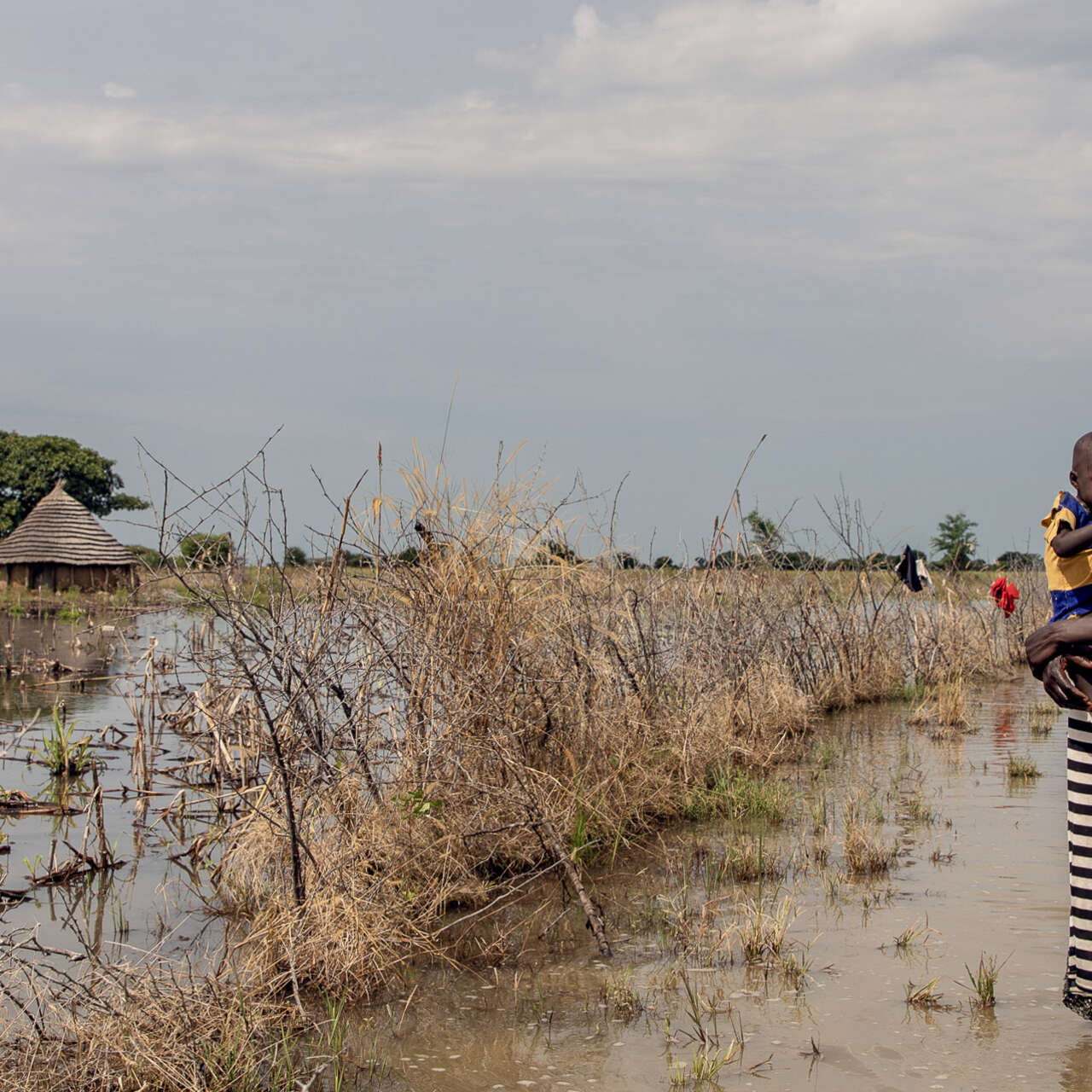 A mother holds her daughter tight to her chest while walking outdoors in a flooded region of South Sudan.