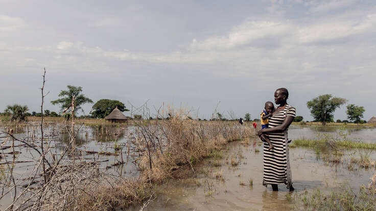 Abuk, holding Nyirou, poses for a portrait in front of their flooded house, in Northern Bahr El Ghazal, South Sudan.