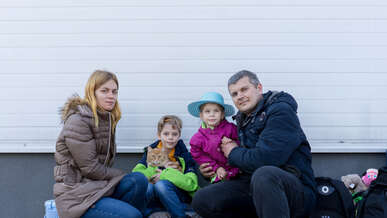 A Ukrainian family poses for a photo outside. A young son holds the family's cat.