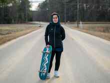 An Afghan refugee poses for a photo while holding her skateboard.