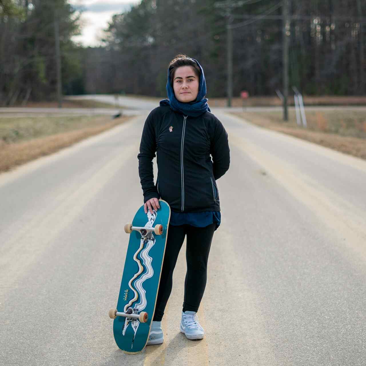 An Afghan refugee poses for a photo while holding her skateboard.