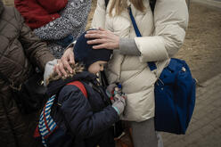 A close up of a young girl leaning against her mother, who places her hands on her back and head. 