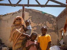 A mother stands with her three children in the ruins of a destroyed building in Sudan.