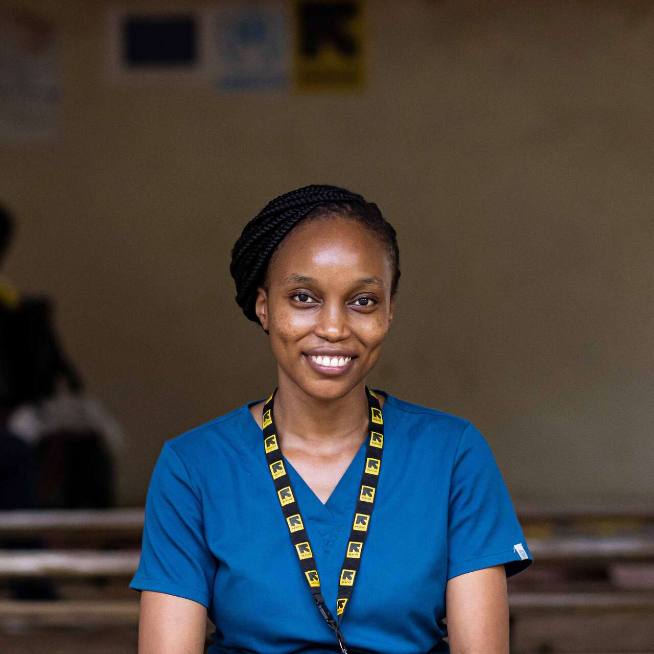 A woman wearing blue nurses scrub and an IRC lanyard, smiles and poses for a photo.