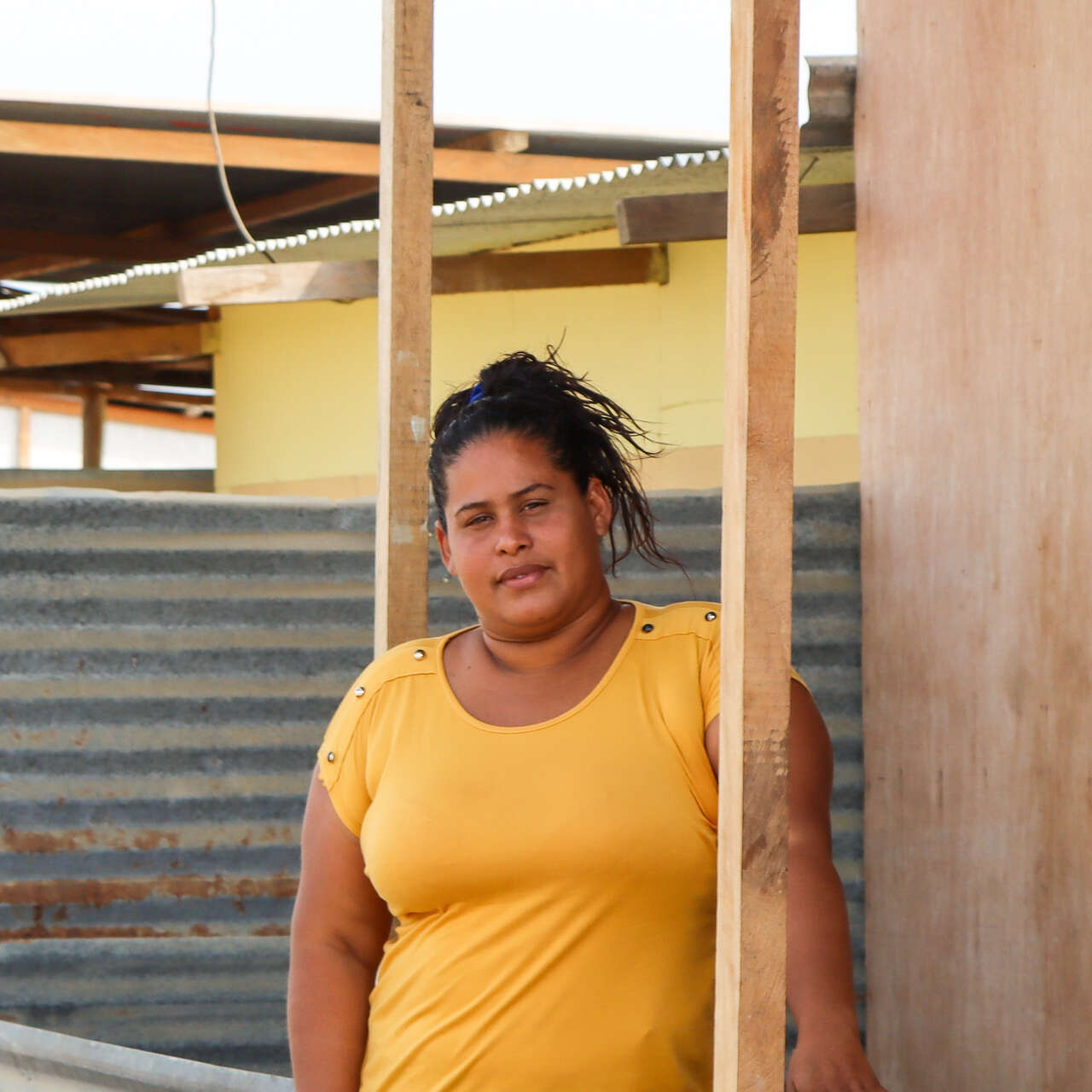 A woman stands outside a makeshift shelter and poses for a photo.