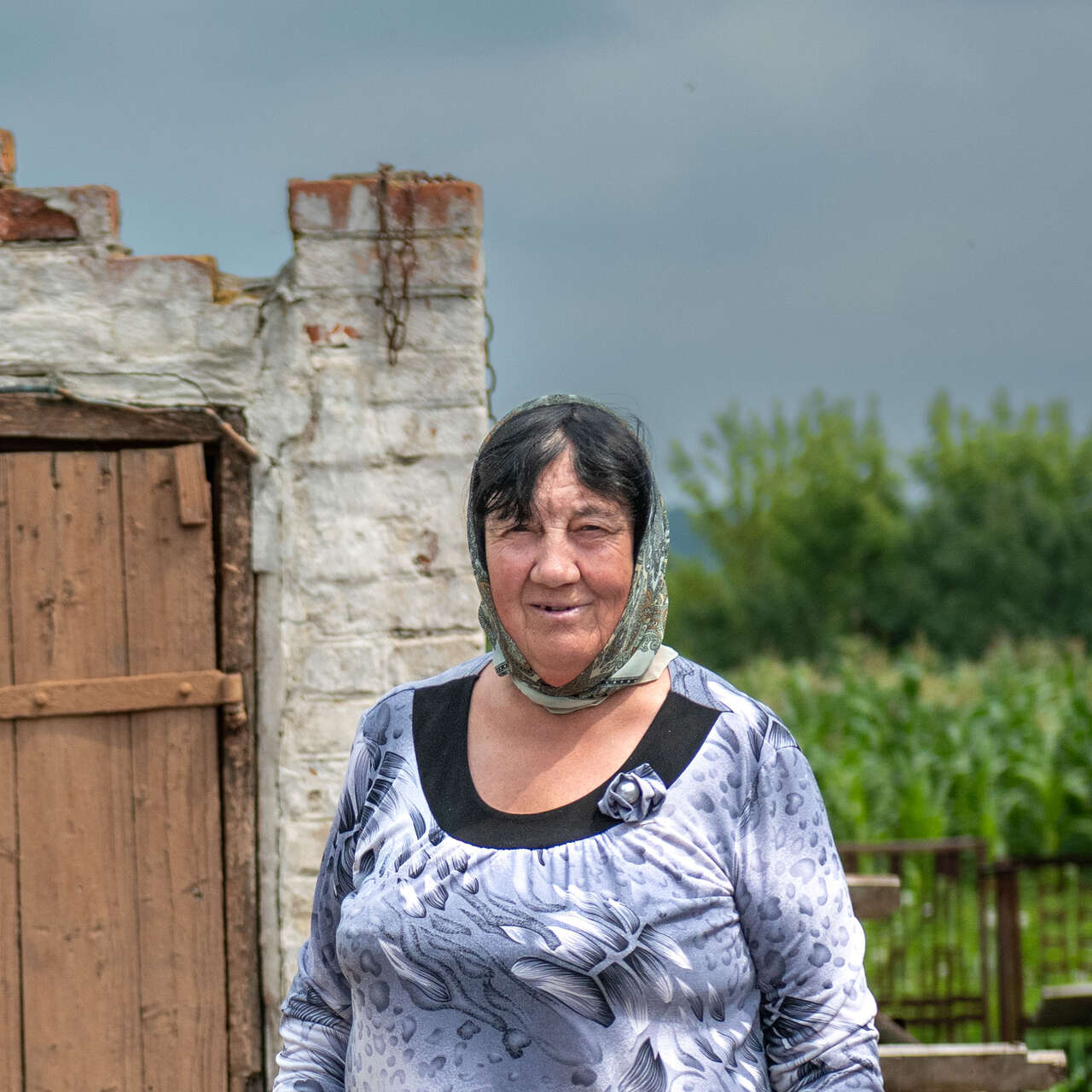 A woman poses for a photo in front of a building destroyed by the war in Ukraine.