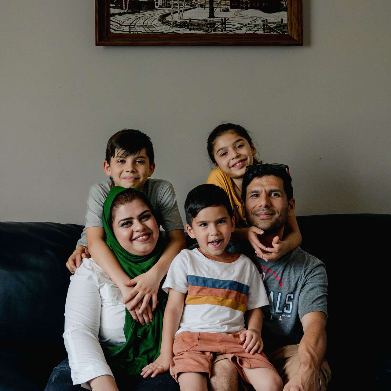 A family sits together on a couch and poses for a photo.