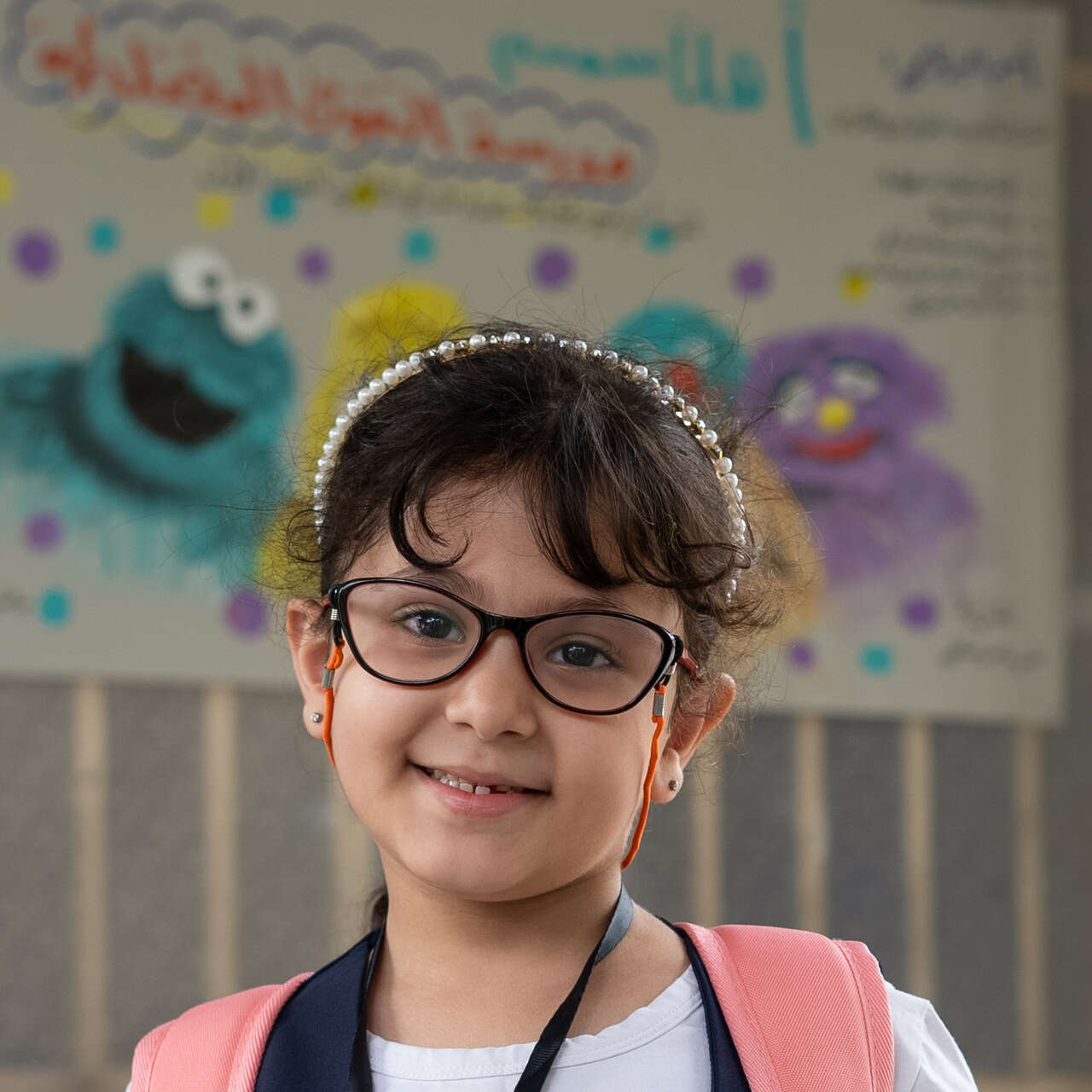 A girl in a classroom smiles and poses for a portrait.