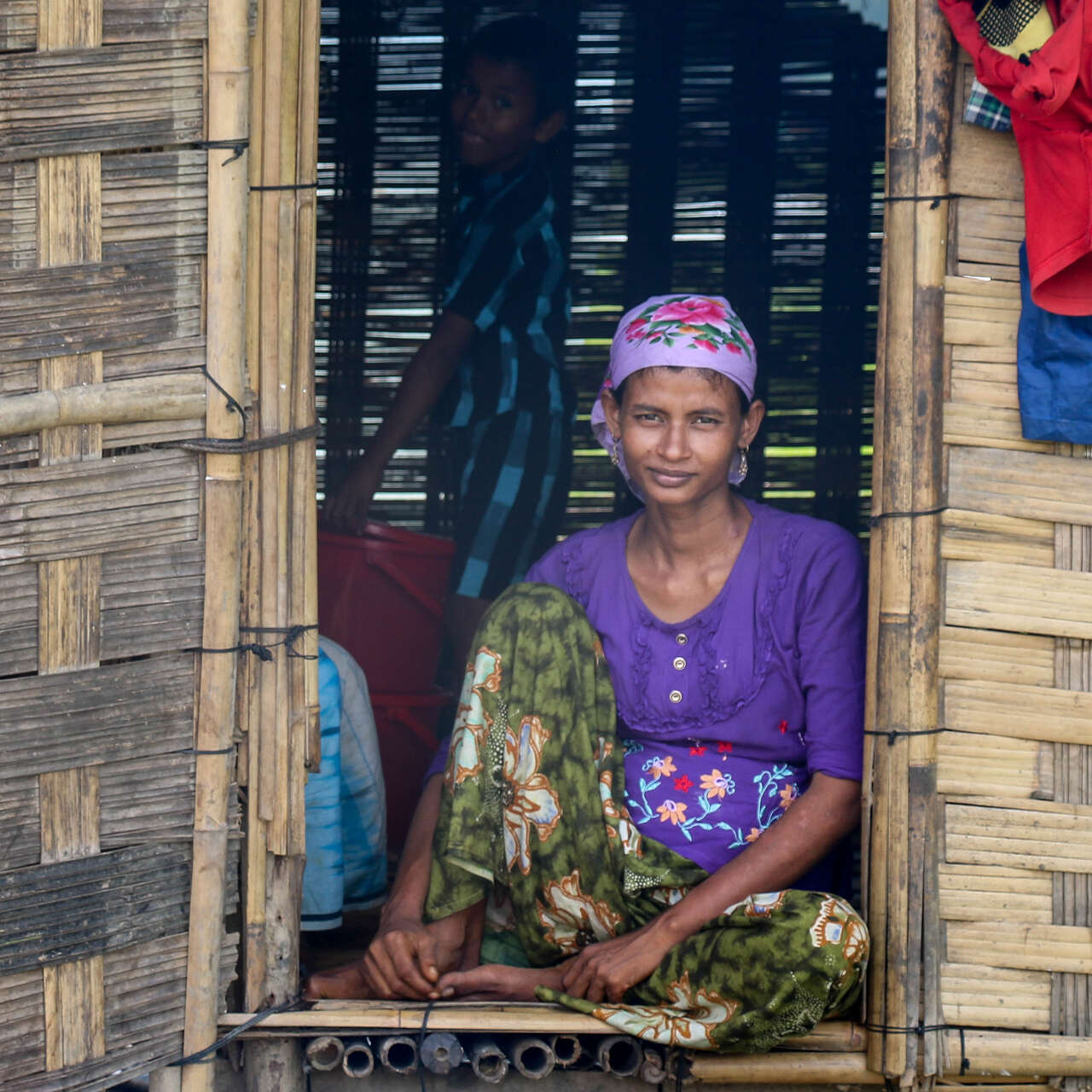 A woman sits in the doorway of her home in Myanmar and poses for a photo.