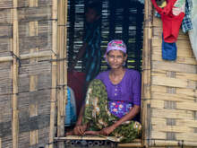 A woman sits in the doorway of her home in Myanmar and poses for a photo.