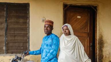 A man and a woman pose for a portrait while sitting atop a motorbike.