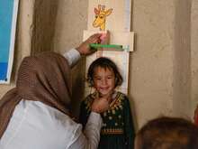 A smiling child in Afghanistan has their height measured.