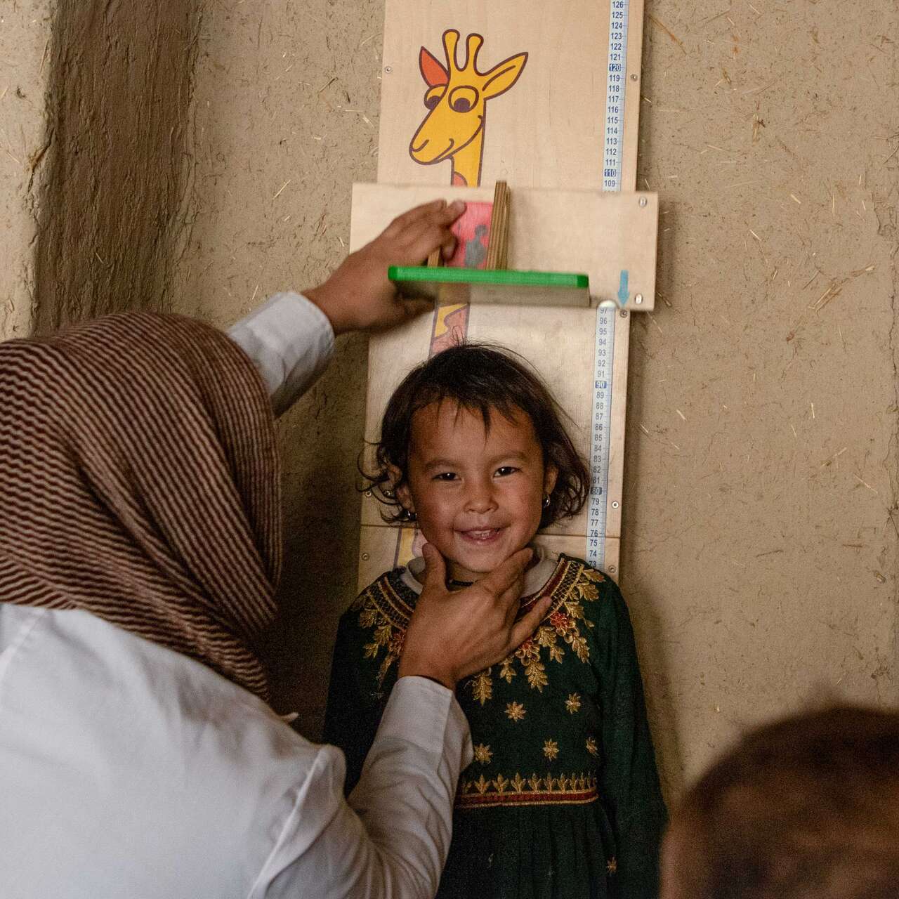 A smiling child in Afghanistan has their height measured.