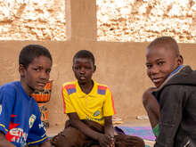 Three boys sit on the floor together in conversation. They look towards the camera.