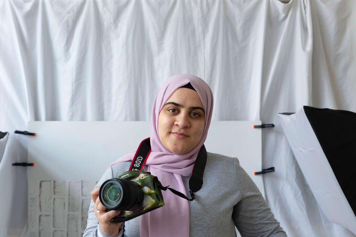 Hamida smiles, holding her camera in her hand.