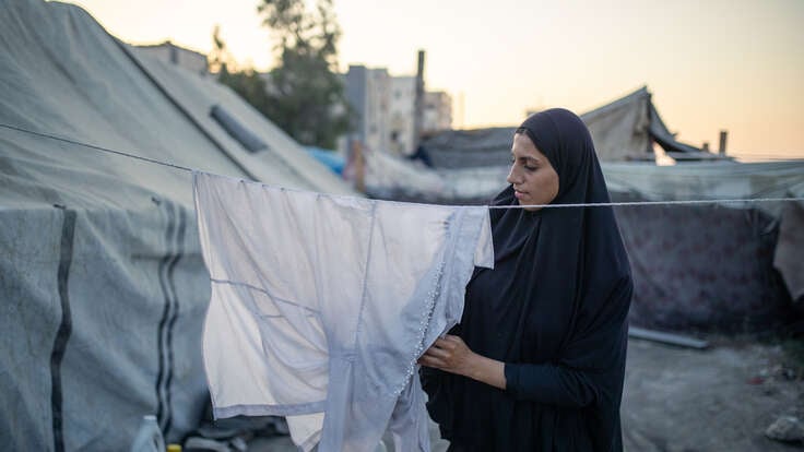 Tjej i Gaza hänger kläder på en tvättlina, tält syns i bakgrunden.