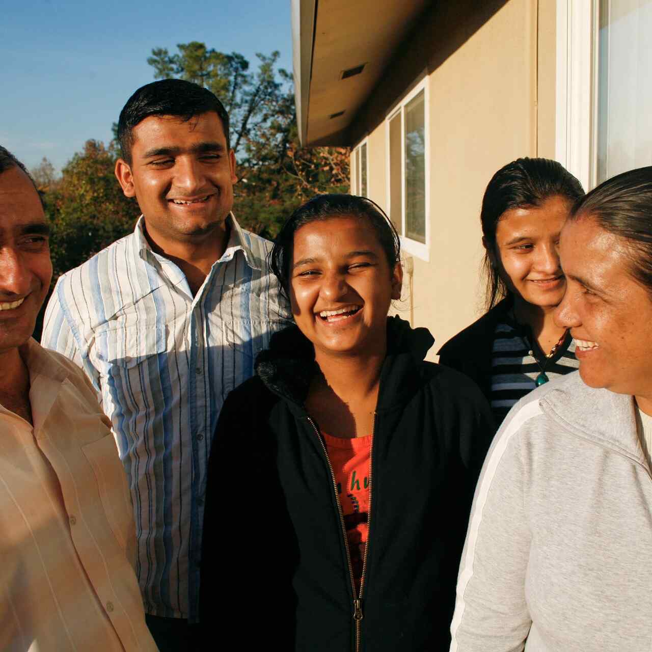 Family of five stands outside its Sacramento home, laughing together while their picture is taken.