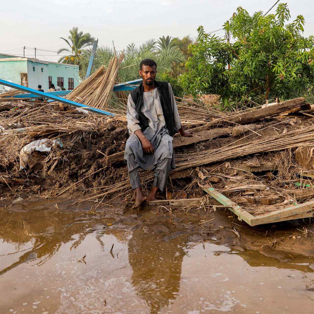 A man sits by a destroyed shack in a flooded area in Sudan