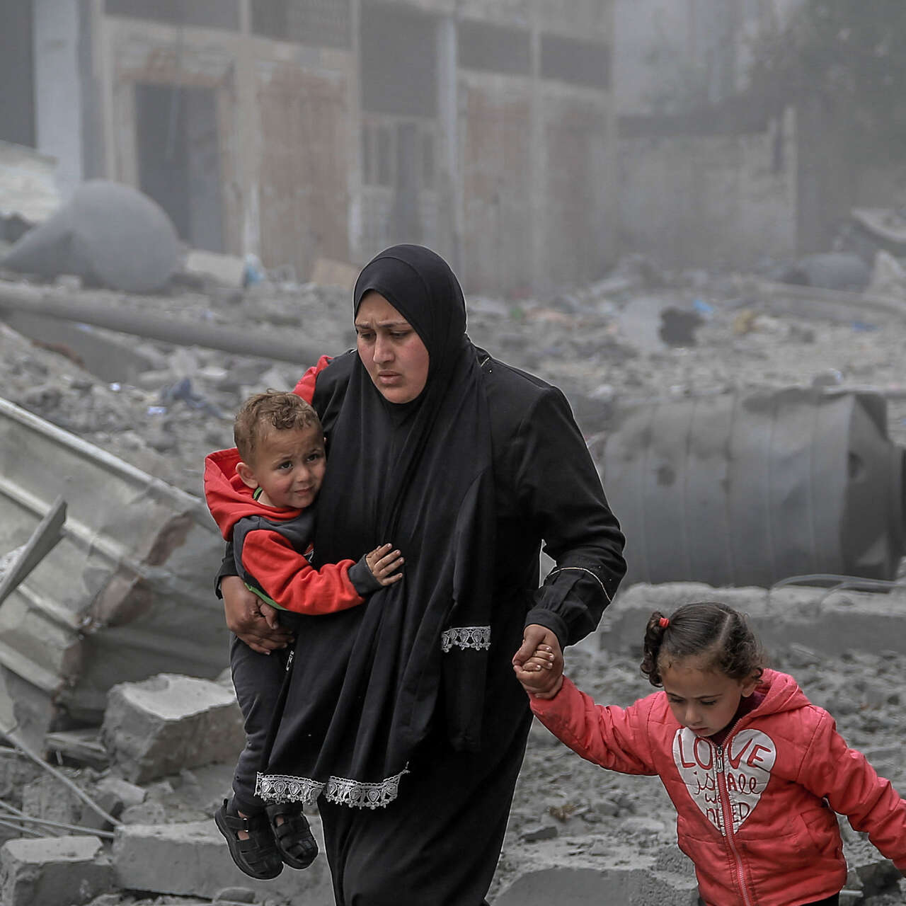 A mother holds her two children while she makes her way through the remnants of a building destroyed by the war in Gaza.