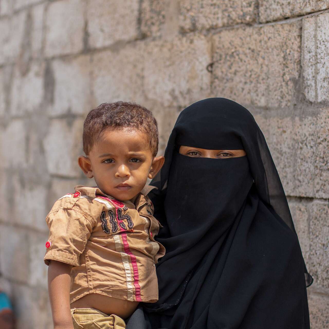 A mother holds her child in her arms. Together, they pose for a photo in Yemen.