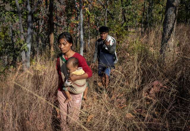 A mother carries her child in a sling and makes her way through a dense forest in Myanmar. Her husband follows behind.