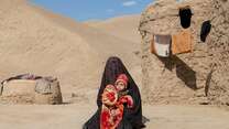 A woman, wrapped in a blanket, holds her young grandson in her arms outside of a clay structure in rural Afghanistan.