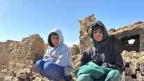 Two Afghan boys sit atop a pile of rubble from a building destroyed by an earthquake.