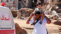 A man holds a boy high on his shoulder while walking through Derna, Libya after the flooding.