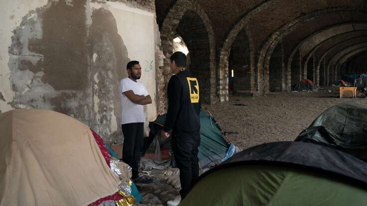 An IRC officer speaks with an asylum seeker in Italy. They stand nearby a series of tents.