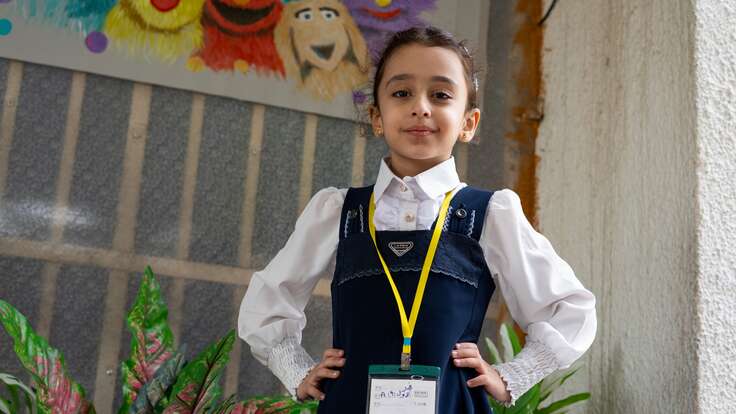 A six year old girl poses for a photo, sporting a soft smile with her hands on her hips.