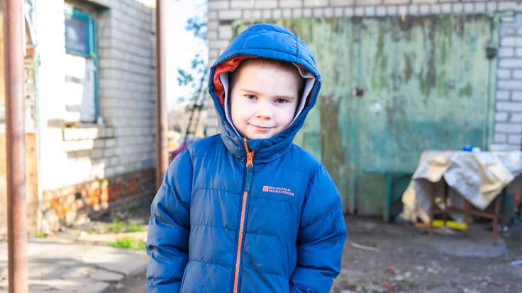 A young boy in a blue jacket poses for a photo, smiling softly at the camera.