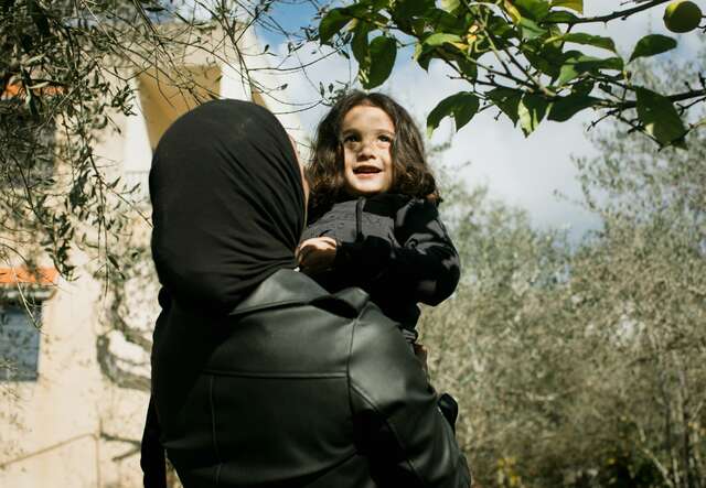 A mother holds her smiling daughter in her arms.