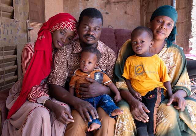 A family of five sits on a couch at their home in Burkina Faso and pose for a photo.