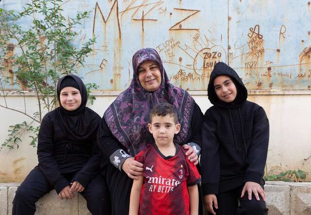 A mother sits outside with her three children. The family has been displaced from their home in Lebanon.