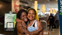 Two women stand and embrace after reunifying at an airport.