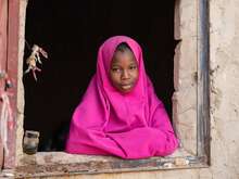 A girl in a pink outfit leans out of a windowsill in Niger.