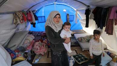 A family in Syria poses for a photo in their makeshift shelter in a refugee camp.