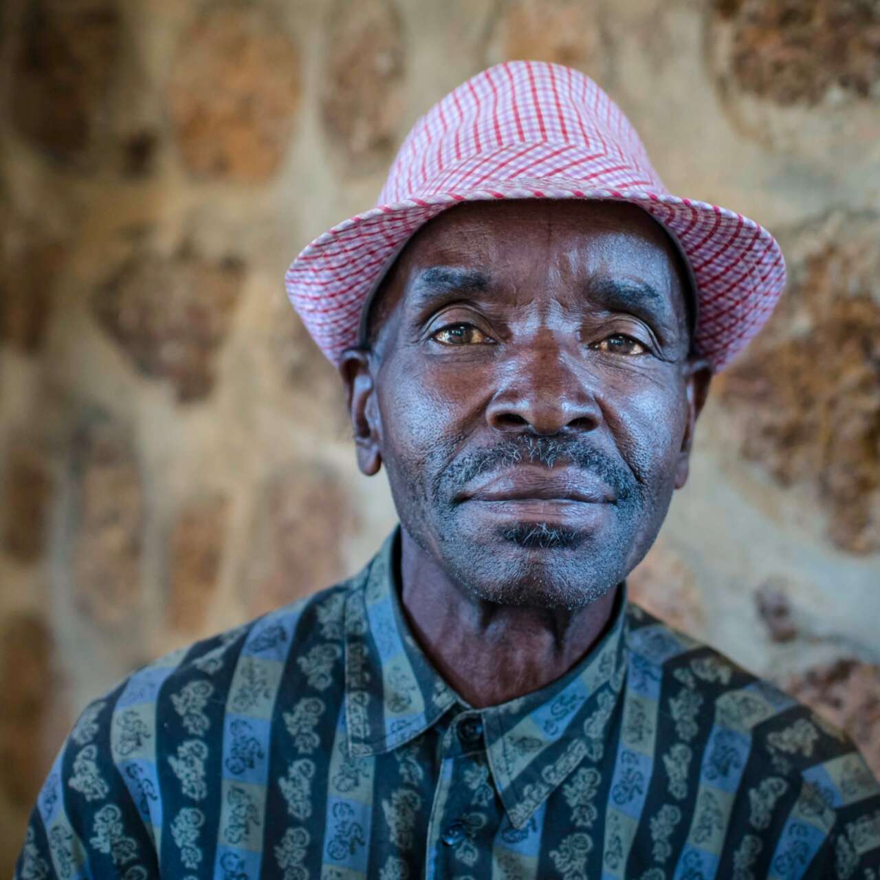 A man wears a red hat and solemnly stares into the camera for a portrait.