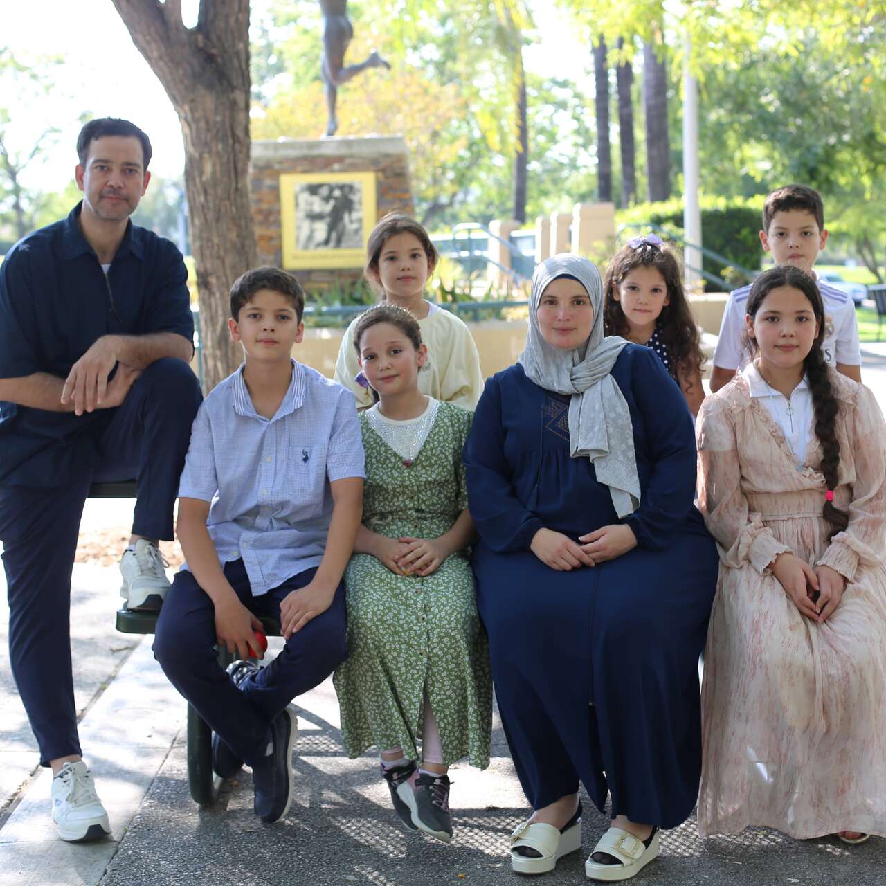 A family of 8, a dad, a mom, and their 2 boys and 4 girls, sit together and pose for a family photo after a Baby Shower event hosted by the IRC-LA office.