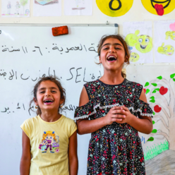 Two young girls singing in a classroom.